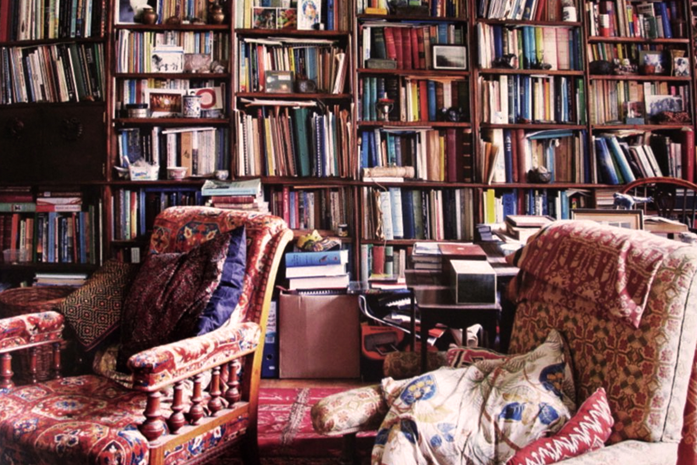 two comfy old chairs with their backs to a wall of floor to ceiling shelves, packed with books